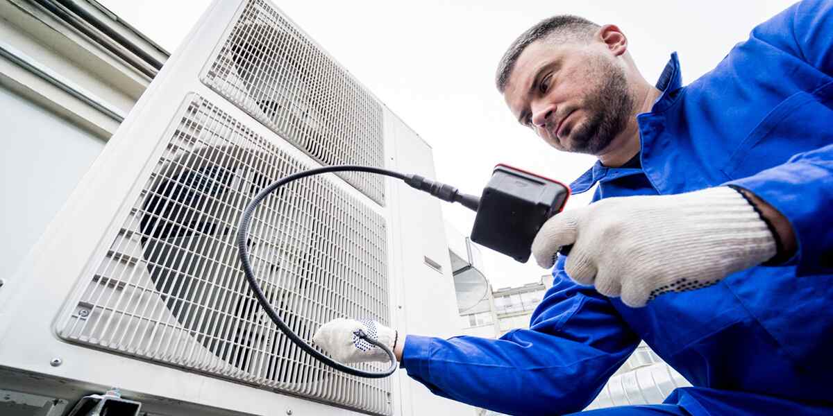 HVAC technician inspecting an outdoor air conditioning unit with a diagnostic tool