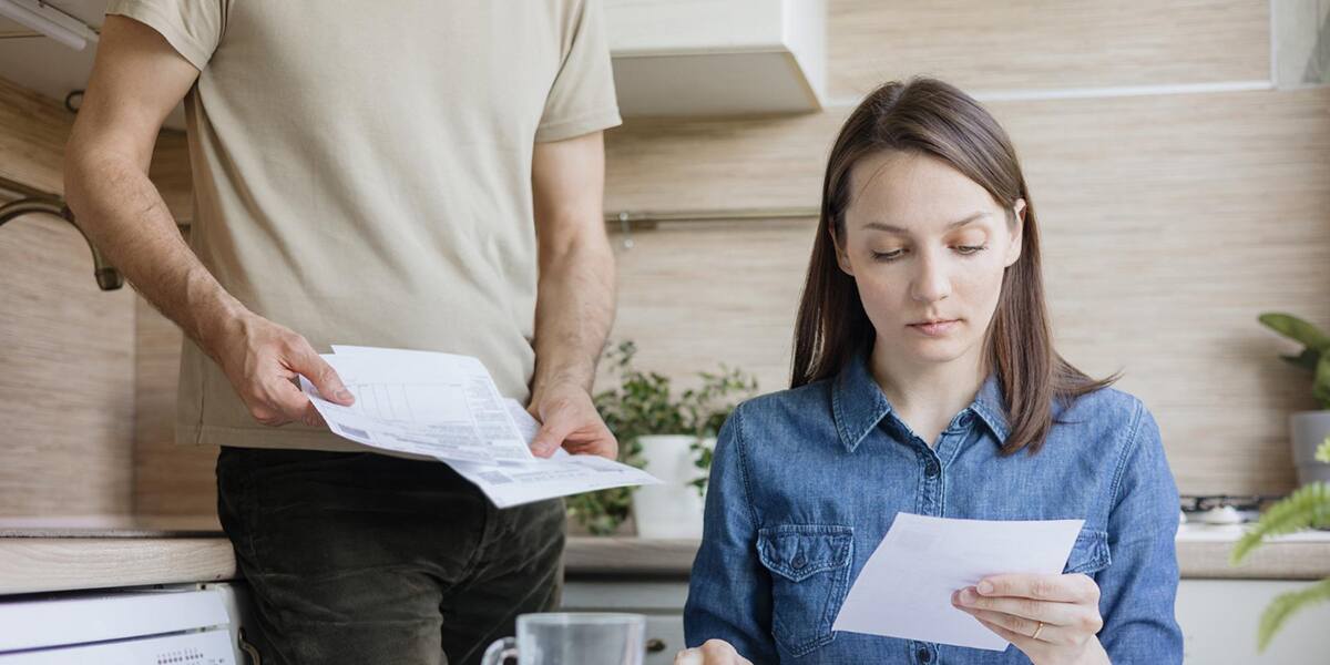 Concerned woman reviewing bills while a man holds documents in the kitchen