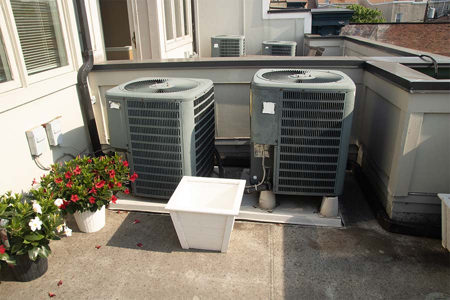 Two outdoor HVAC units on a rooftop with potted plants nearby