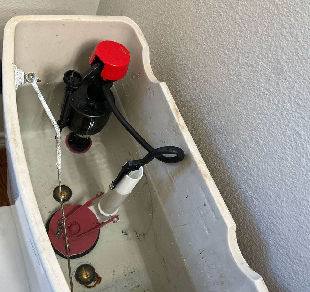 Open toilet tank showing the fill valve, flush valve, and flapper